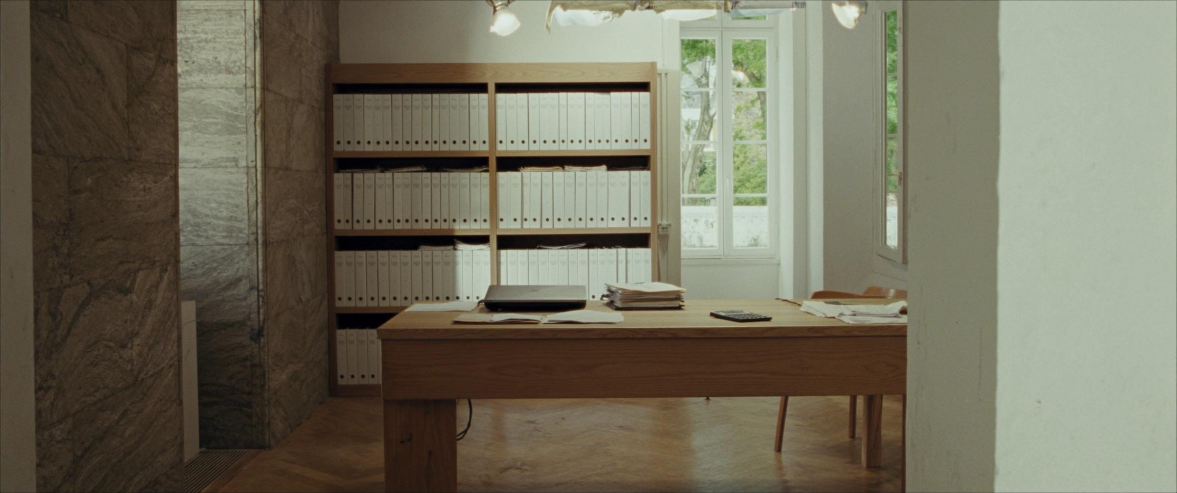 Das Büro eines Treuhänders: ein langer Eichentisch, Dokumentenstapel, Ordner in Reihen auf Holzregalen, hohe Fenster.
