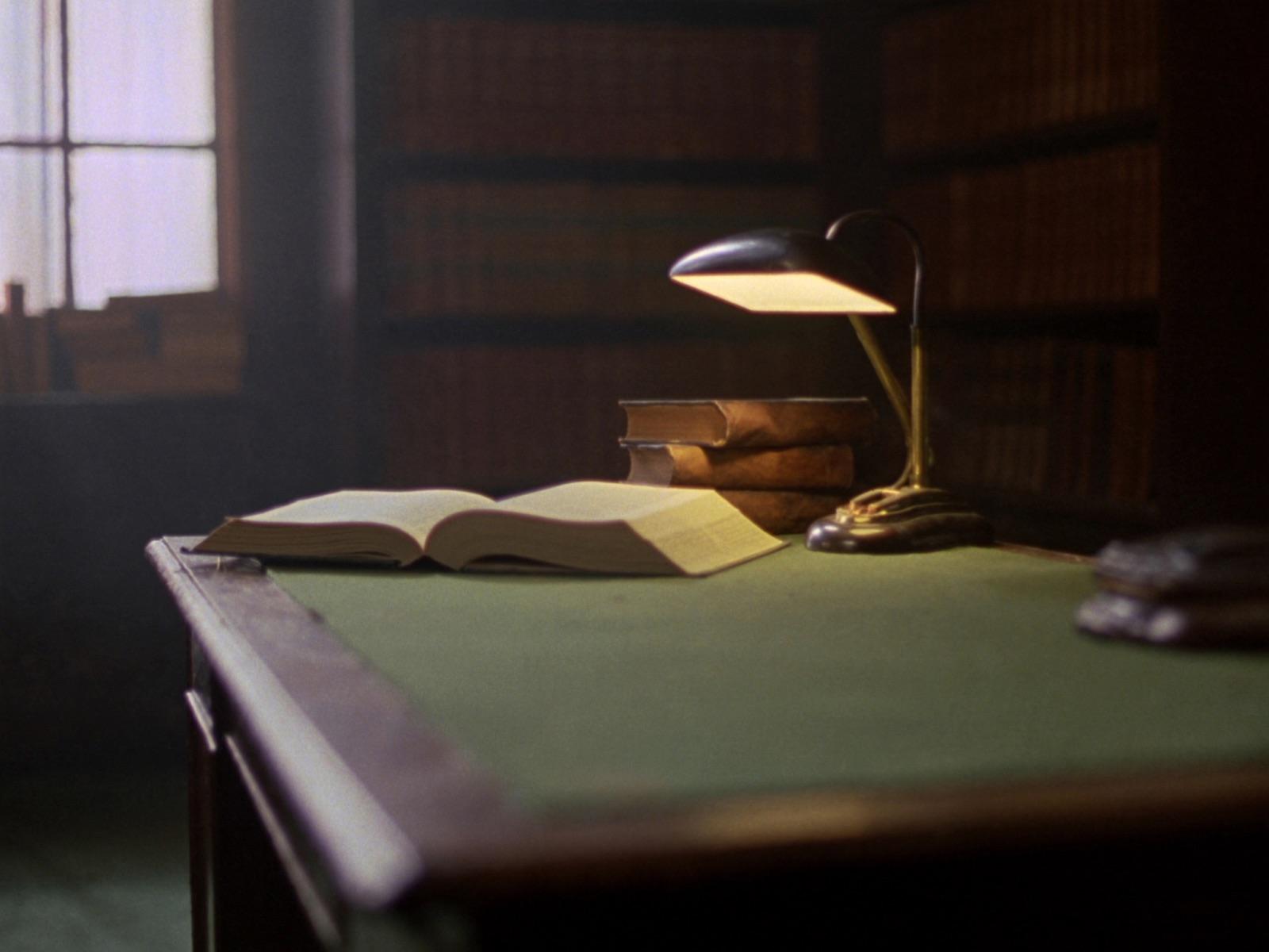 Ein Lesetisch in einer juristischen Bibliothek: ein aufgeschlagener Band und ein Stapel gebundener Gesetzbücher unter einer Messinglampe.